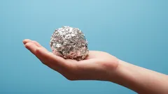 Ruka držící kouli z alobalu před modrým pozadím