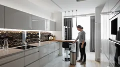 Moderní kuchyně s lesklými skříňkami a člověkem u stolu v minimalistickém interiéru.
