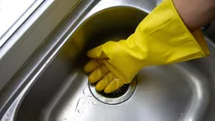 Čištění dřezu rukou v gumové rukavici, domácí úklid kuchyně
