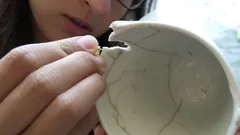 Oprava rozbité keramické misky metodou kintsugi, detail ruky a zlaté linky na keramice.