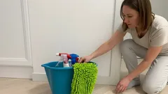 Žena s vědrem, mopem a čisticími prostředky připravena na úklid podlahy.
